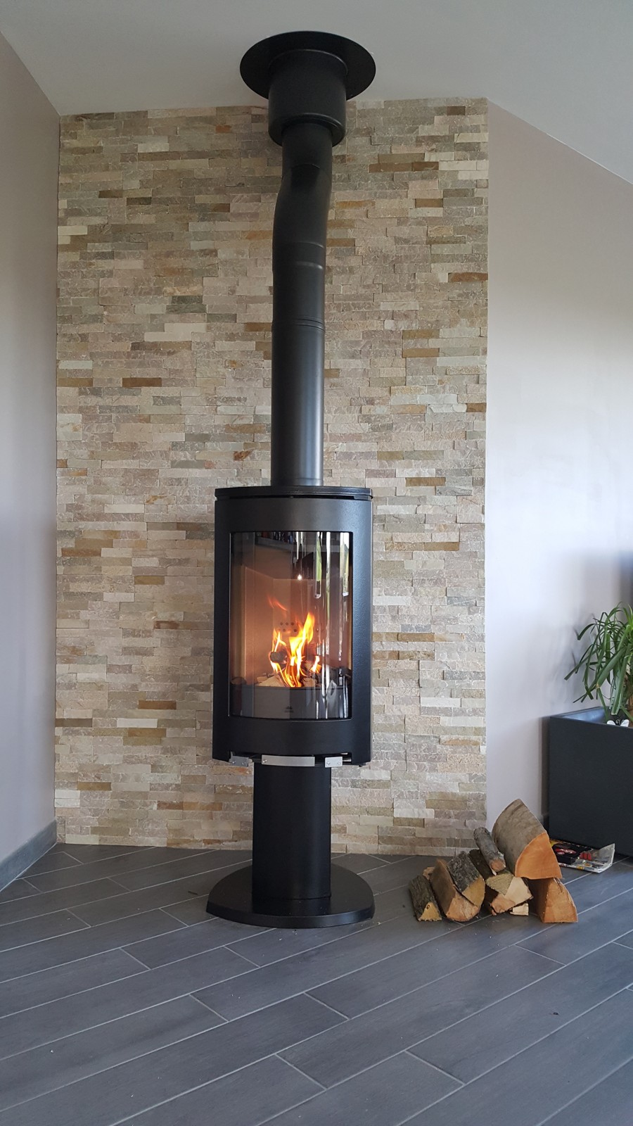 Jotul F 373 freestanding pedestal wood stove against a stone feature wall